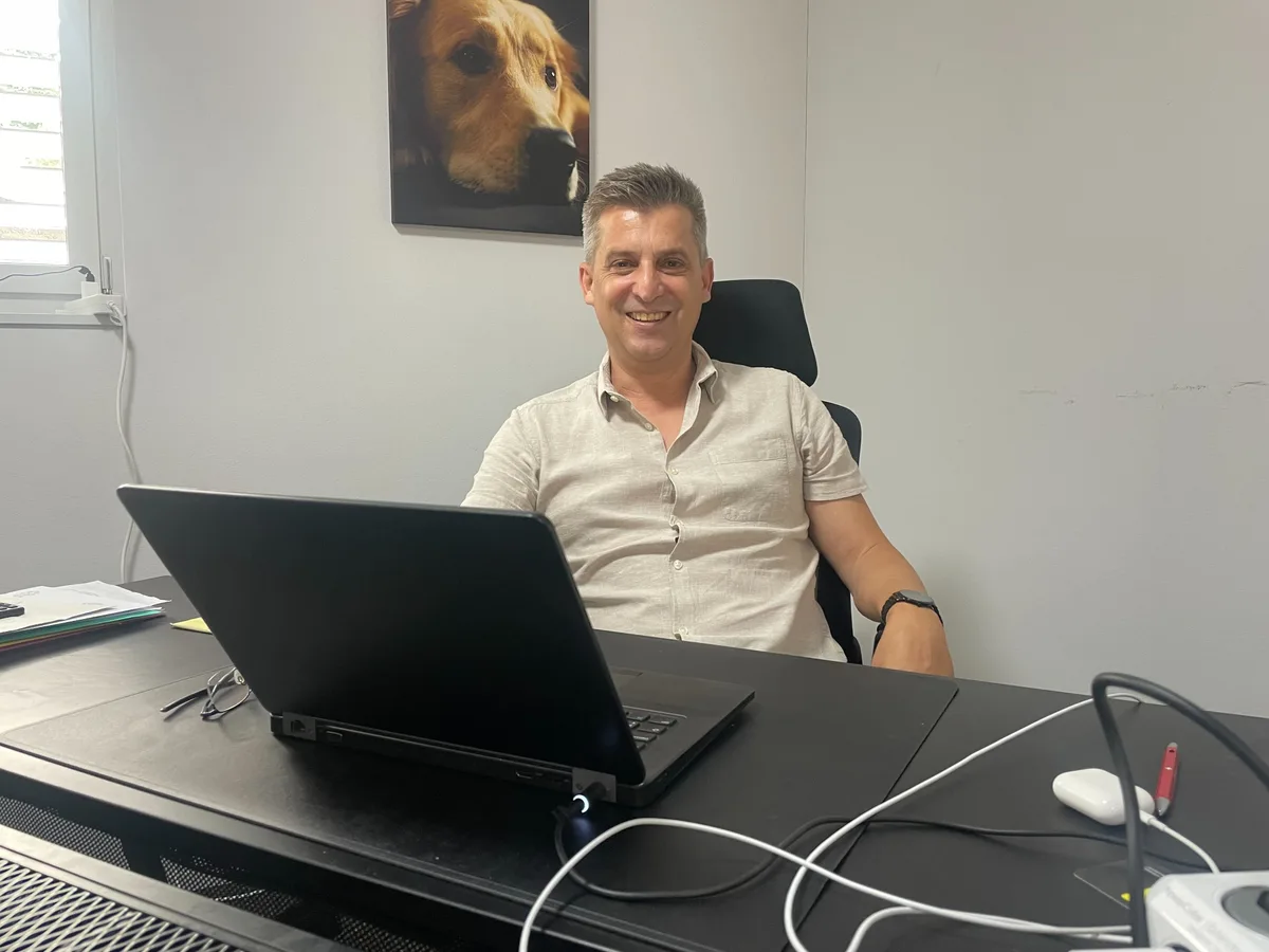 Jonny Billeter in seinem Büro in Mönchaltorf. Mann sitzt an Laptop an seinem Schreibtisch und lacht in die Kamera.